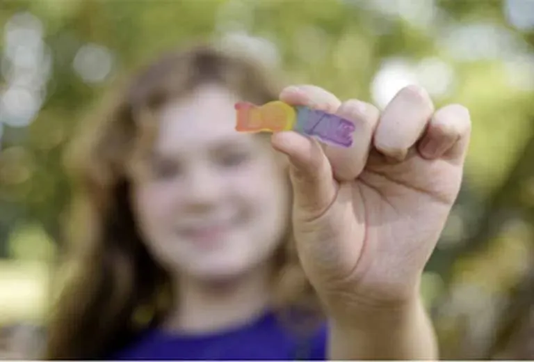 Ein Kind hält ein regenbogenfarbenes Gummibärchen in die Kamera